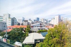 A cityscape with a mix of modern and traditional buildings, including a prominent multi-story structure with a flat roof and a smaller building with a sloped roof. - Sio R-Suite (Seoul)