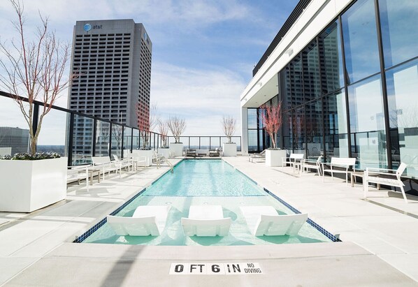 A rooftop pool with a depth marker of 6 feet, surrounded by white lounge chairs and modern buildings in the background.