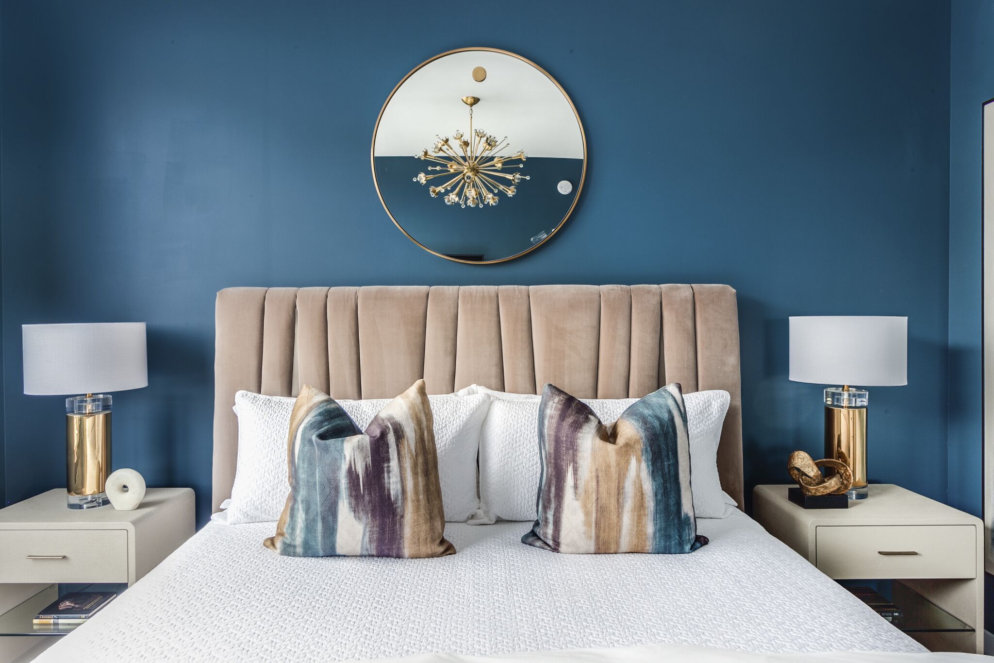 A bedroom with a tufted headboard, two bedside tables with lamps, and a large round mirror on the wall.