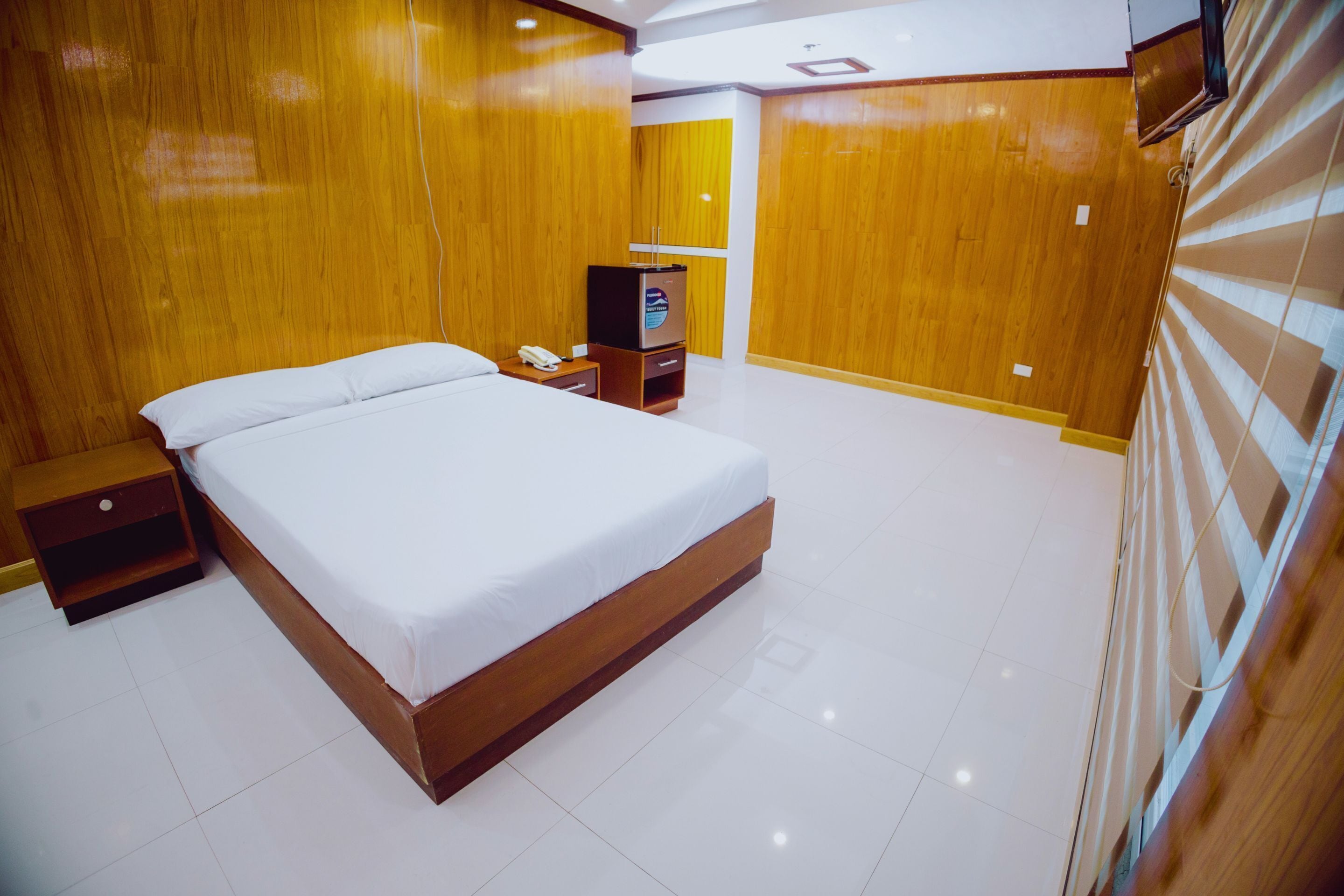 A hotel room with a large bed, wooden walls, a small bedside table with a phone, and a television on a stand.