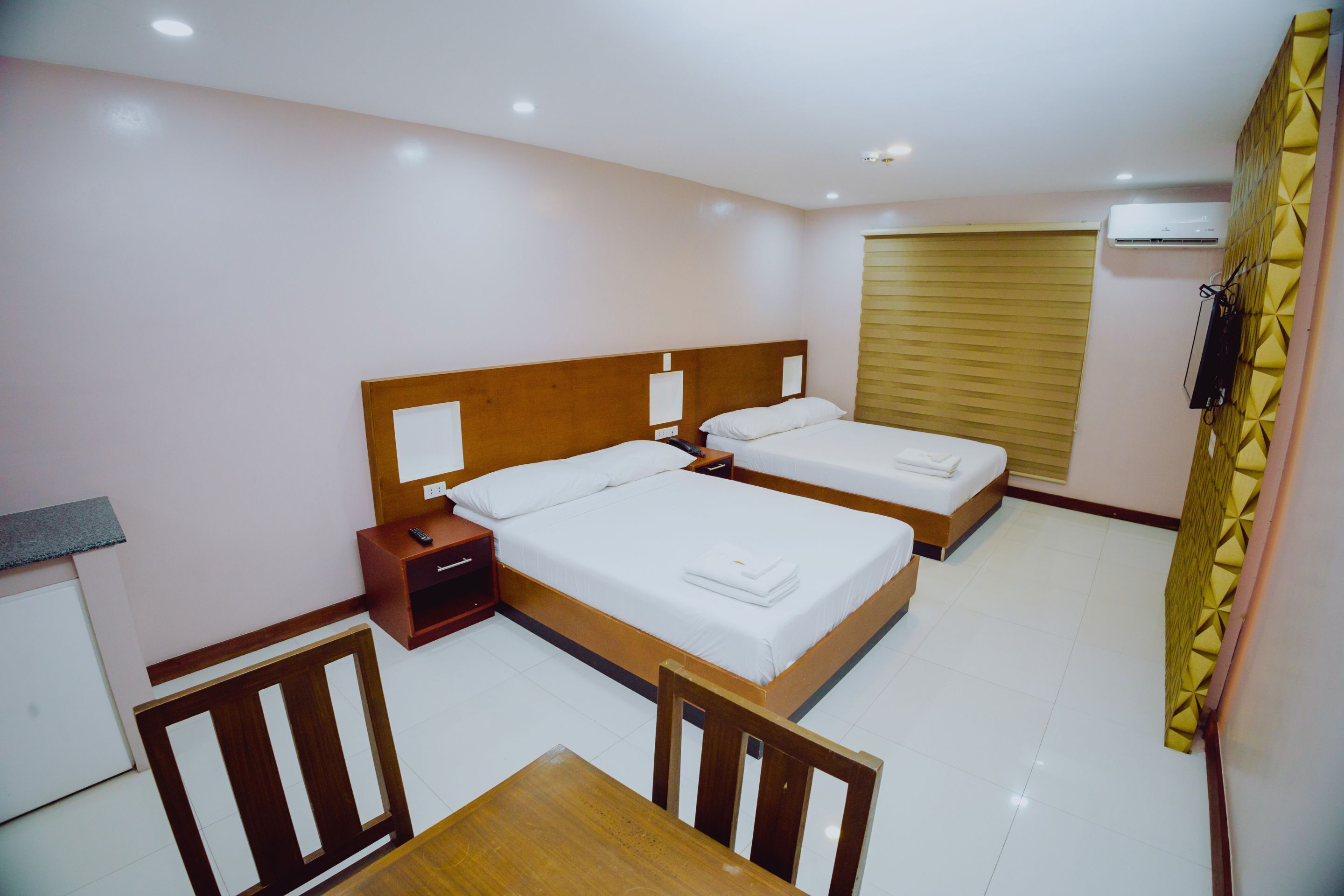A hotel room with two beds, a wooden table, and a small desk with a chair.