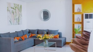 A modern living room with a grey sofa, a glass coffee table, and a vase with yellow flowers. - Coastal Hotel Iloilo (Leganes)