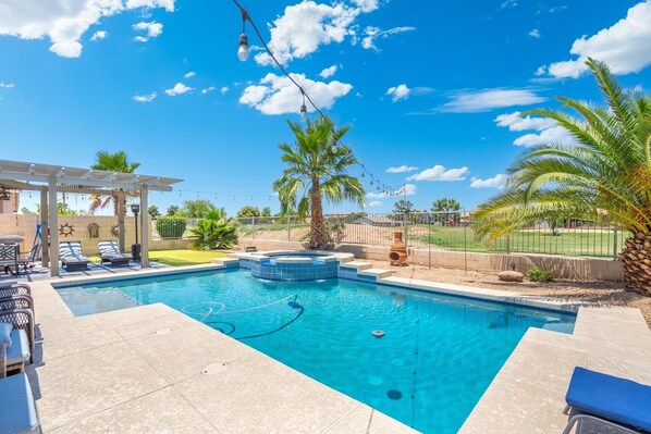 A swimming pool with a hot tub, lounge chairs, and a pergola.