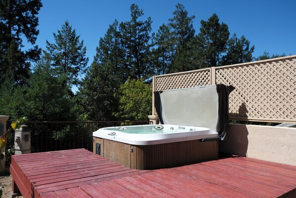 Un jacuzzi en una terraza de madera con un cerramiento de celosía al fondo.