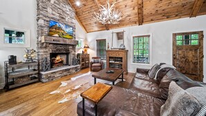Un salon chaleureux avec une cheminée en pierre, un canapé en cuir, une table basse en bois et un lustre.