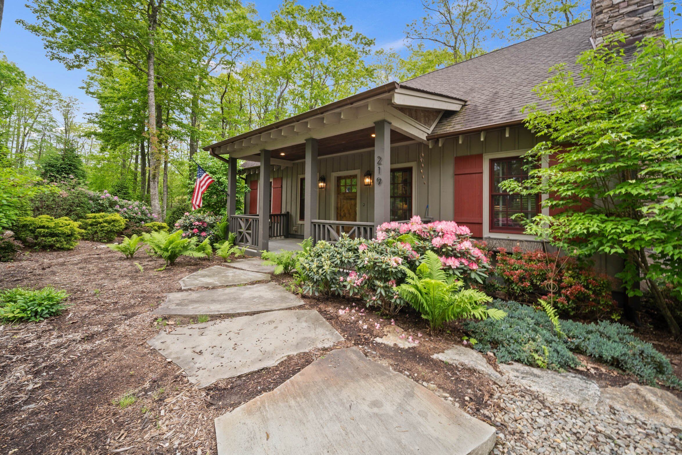 A house with a porch, surrounded by a garden with various plants and flowers.