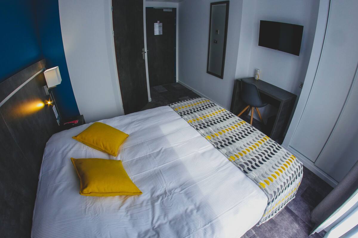 A hotel room with a bed, a bedside table, a chair, a TV, and a door.