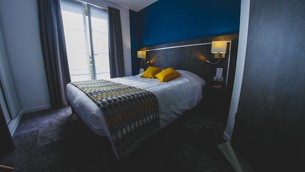 A hotel room with a bed, a nightstand, a lamp, and a window with curtains. - Hôtel du Tramway (Laon)