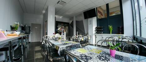 Un moderno comedor con varias mesas y sillas, una zona de cocina al fondo y vistas al exterior a través de amplios ventanales.