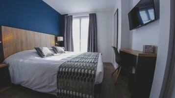 A hotel room with a large bed, a TV mounted on the wall, and a desk with a chair.