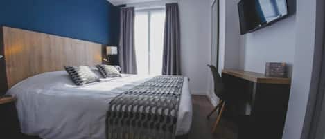 Habitación de hotel con una cama grande, un televisor montado en la pared y un escritorio con una silla.