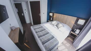 Hotelkamer met een groot bed, nachtkastje met lamp, houten hoofdeinde en uitzicht op de gang.