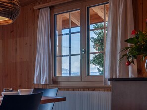 A wooden cabin interior with a dining table, chairs, a radiator, and a window with curtains. - Chalet Dominique by Interhome (Nendaz)