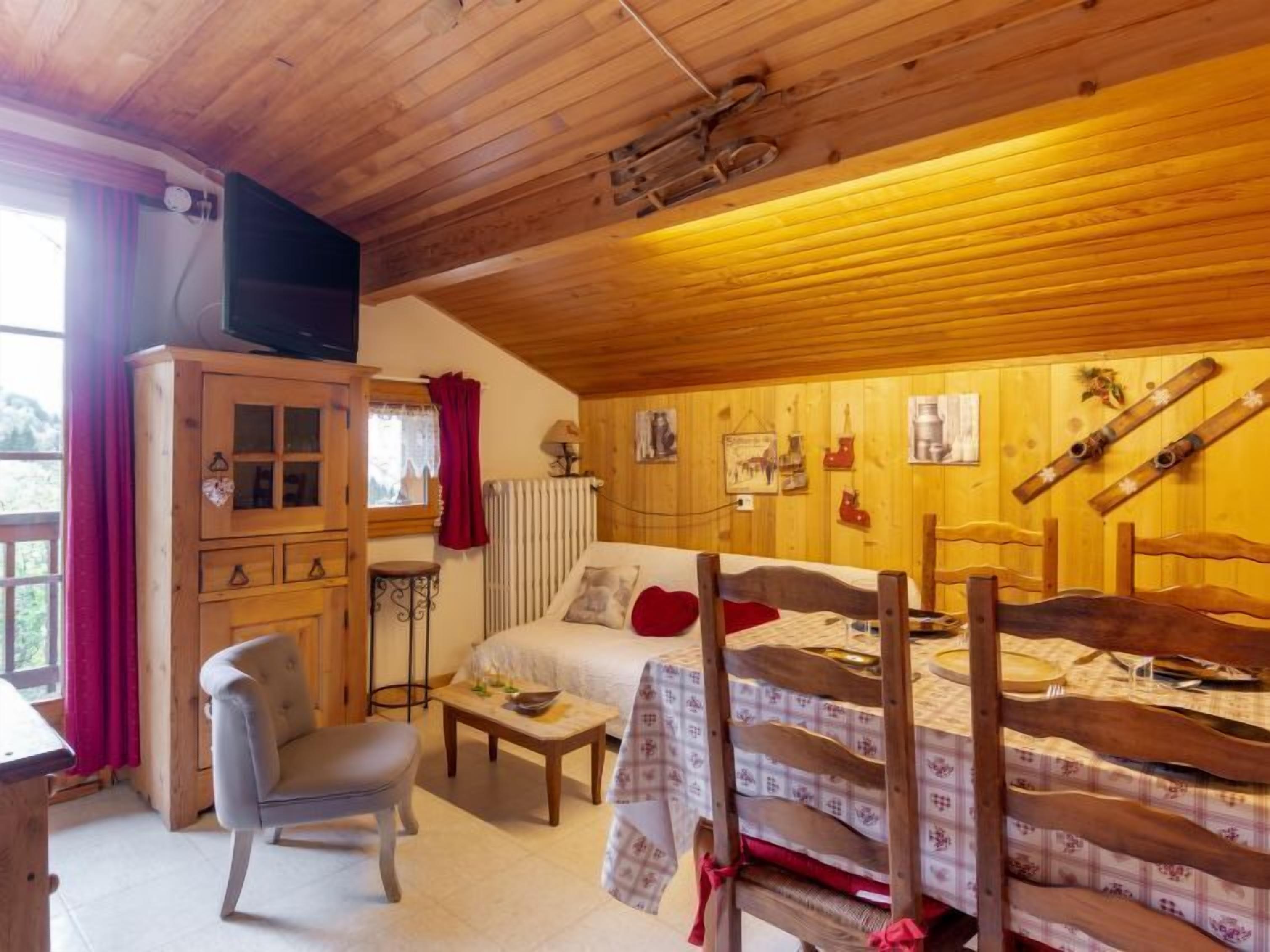Een knus houten kamer met een bed, een stoel, een klein tafeltje en een televisie op een kast.
