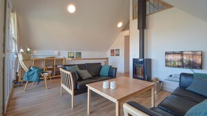Una sala de estar amplia con techo alto, chimenea, sofá, mesa de centro y televisor montado en la pared.