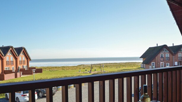Propiedad costera con vistas al mar, que cuenta con una terraza de madera y una mesa con una botella y una copa.