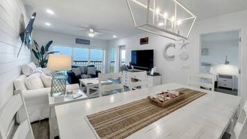 A modern living room with a white sofa, a dining table, and a kitchen area.