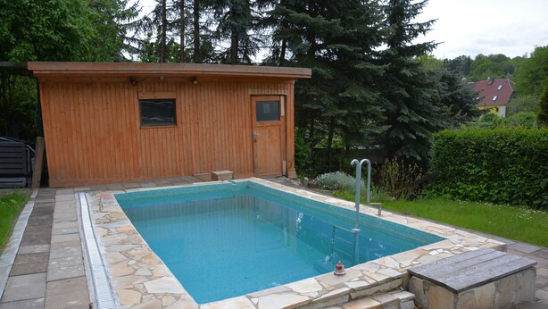 A rectangular swimming pool with a stone border, a wooden deck, and a small wooden building with two windows and a door. - Living in the countryside (Dresden)