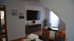 A dining area with a table set for two, a television mounted on the wall, and a potted plant. - Living in the countryside (Dresden)