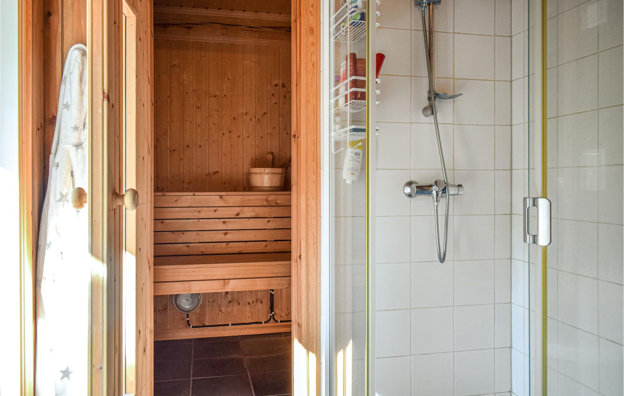 A sauna room with wooden benches, a wooden bucket, and a shower area with a hose and showerhead.