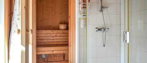 A sauna room with wooden benches, a wooden bucket, and a shower area with a hose and showerhead.