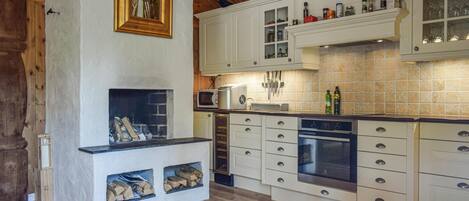A kitchen with white cabinets, a built-in microwave, a stove, and a fireplace with wood logs.
