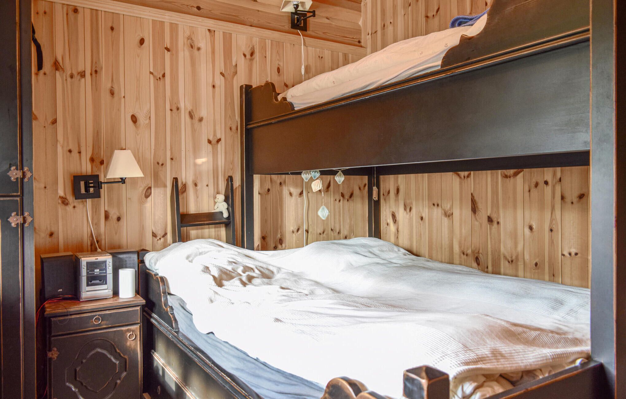 Une pièce aux murs lambrés, avec un lit superposé, une table de chevet avec une lampe et une petite commode.