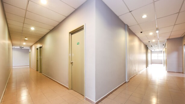 A long, empty hallway with tiled floors and white walls, featuring several doors and a ceiling with recessed lighting. - OYO 89676 Hotel 22 (Seremban)