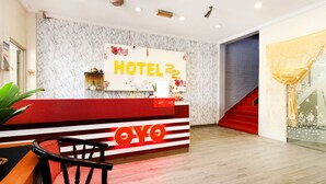 A hotel reception area with a marble wall, a reception desk, a staircase, and a plant. - OYO 89676 Hotel 22 (Seremban)