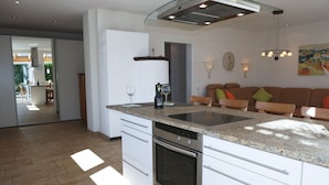 Una cocina moderna con una isla central, horno empotrado y un comedor con mesa de vidrio.