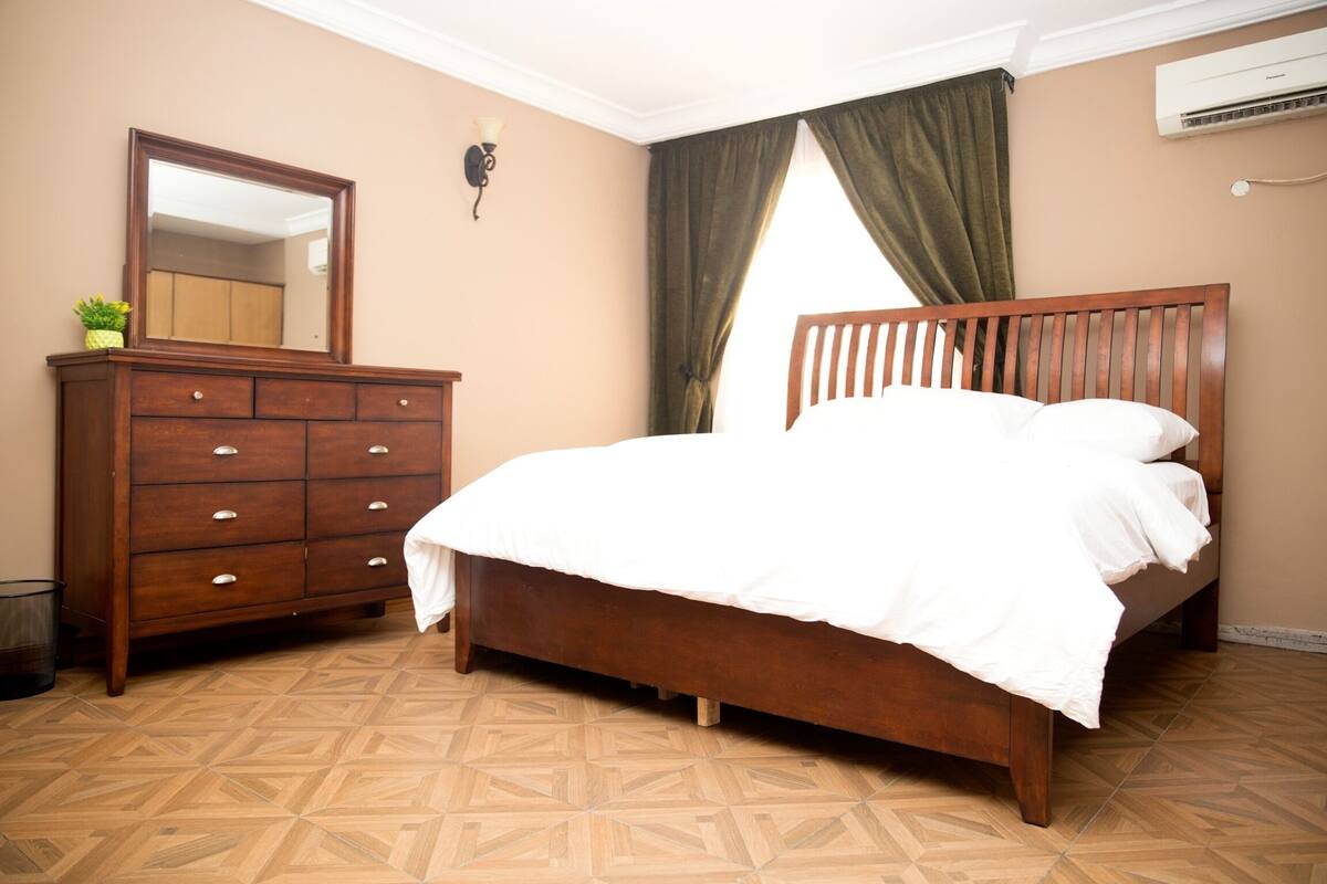 Un dormitorio con una cama de madera, un aparador, un espejo y una ventana con cortinas.