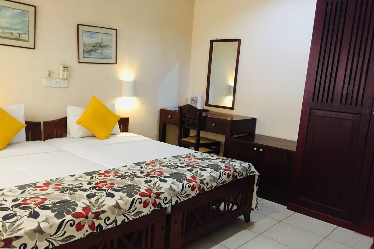 A hotel room with a bed, a desk, a chair, a wardrobe, and a mirror.