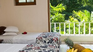 A hotel room with two beds, a balcony with a white railing, and a fruit bowl on the table. - Hotel Sunflower (Kataragama)