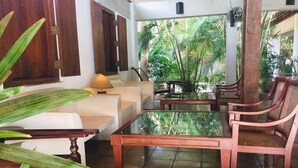 A cozy indoor seating area with a sofa, wooden chairs, and a glass coffee table. - Hotel Sunflower (Kataragama)