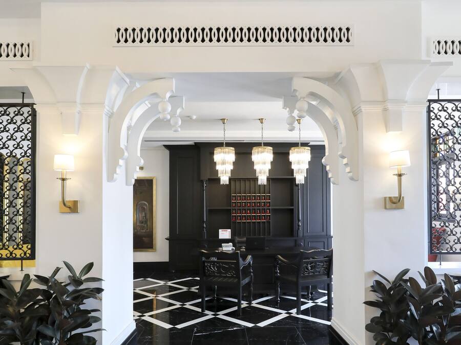 A lobby with a black and white checkered floor, chandeliers, and potted plants.