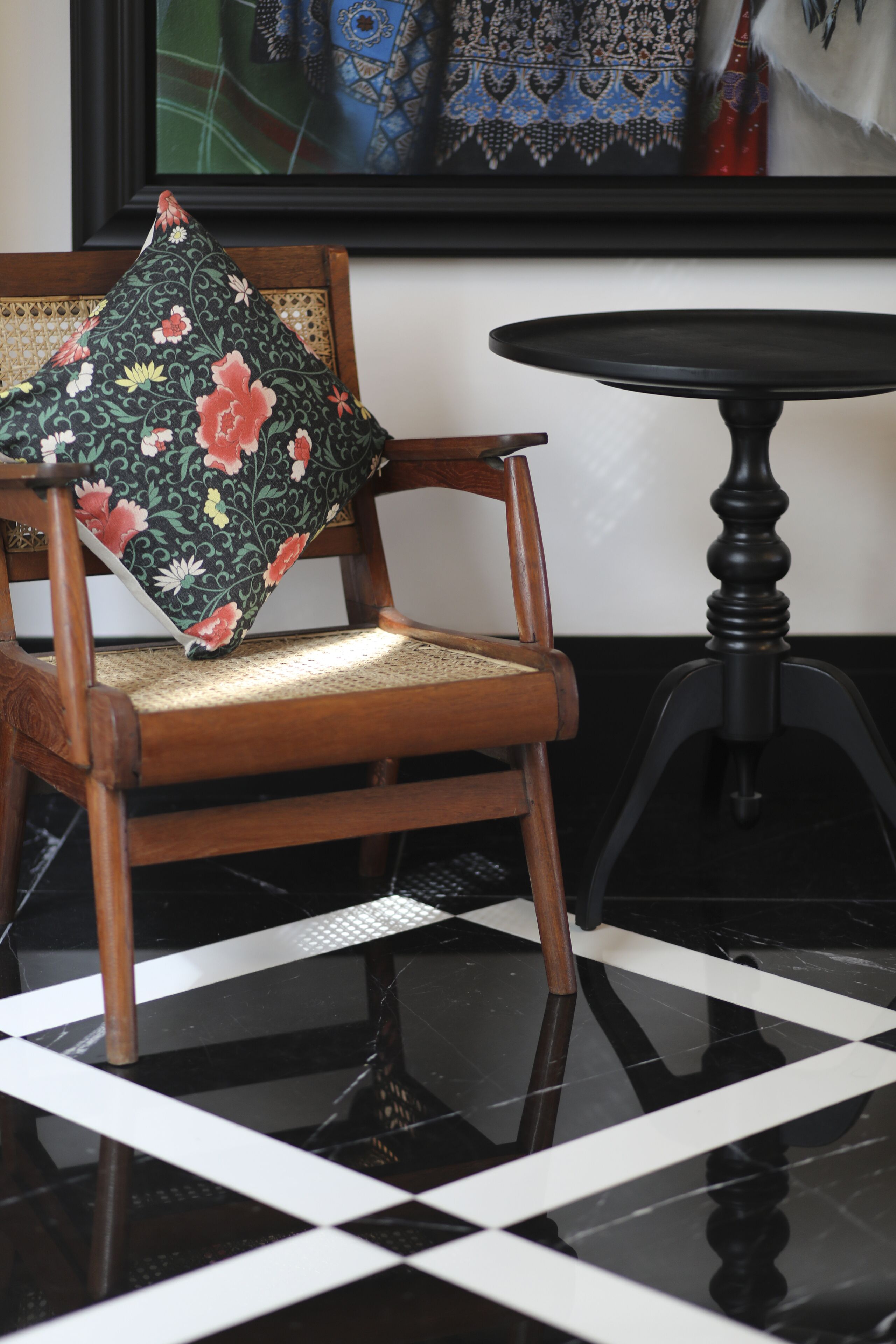 Una silla de madera con un cojín floral, una mesita redonda pequeña y un suelo a cuadros blancos y negros.
