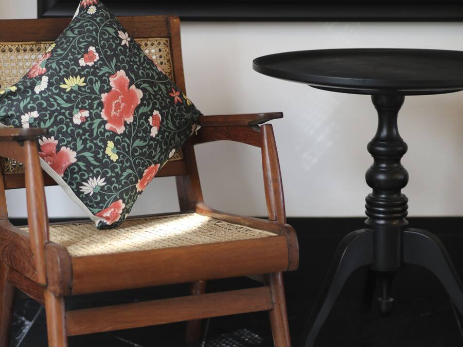Una silla de madera con un cojín floral, una mesita redonda pequeña y un suelo a cuadros blancos y negros.
