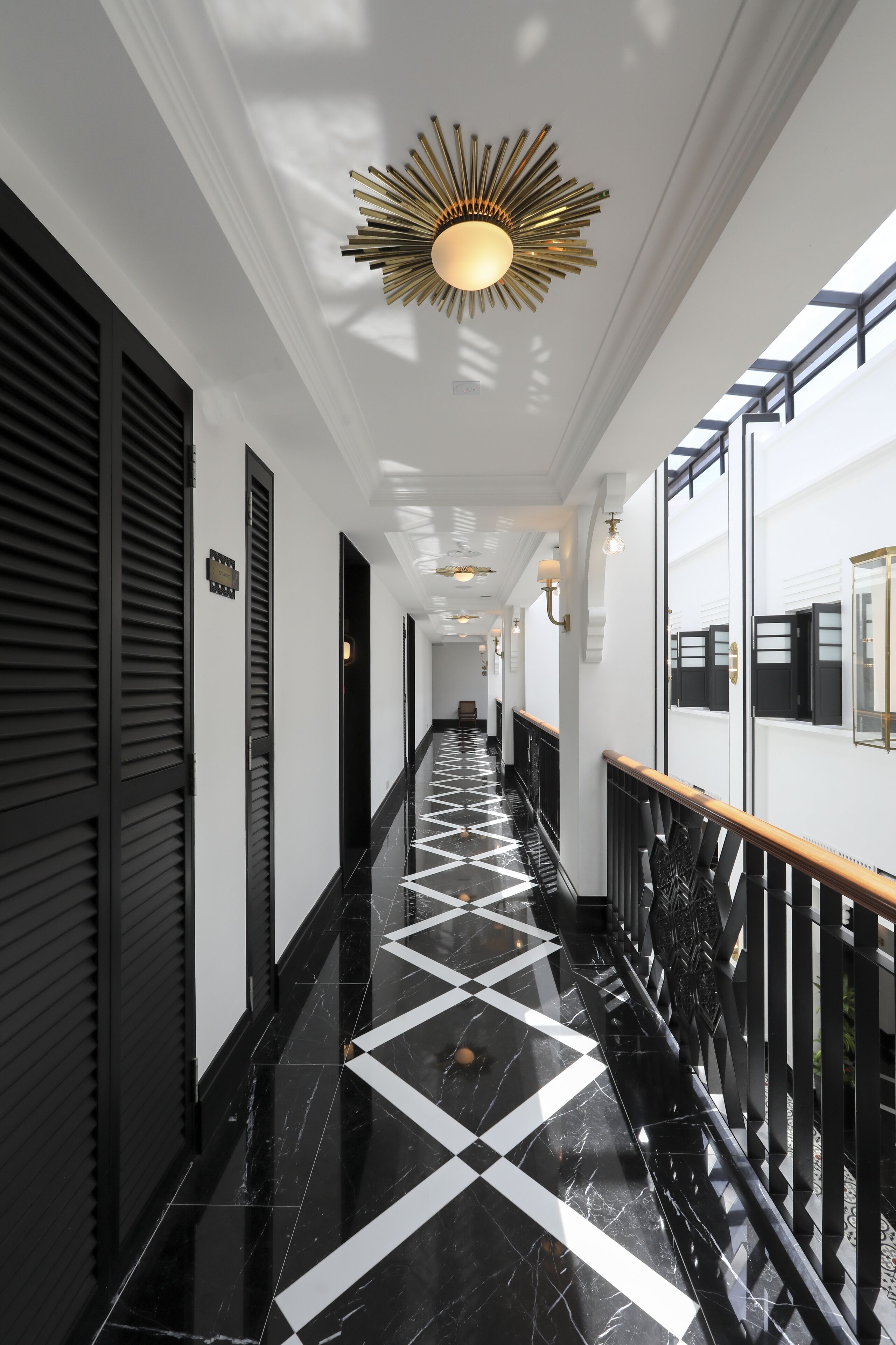 Ein Korridor mit einem schwarz-weiß kariertem Boden, schwarzen Fensterläden und einer Deckenleuchte im Sonnenstrahlendesign.