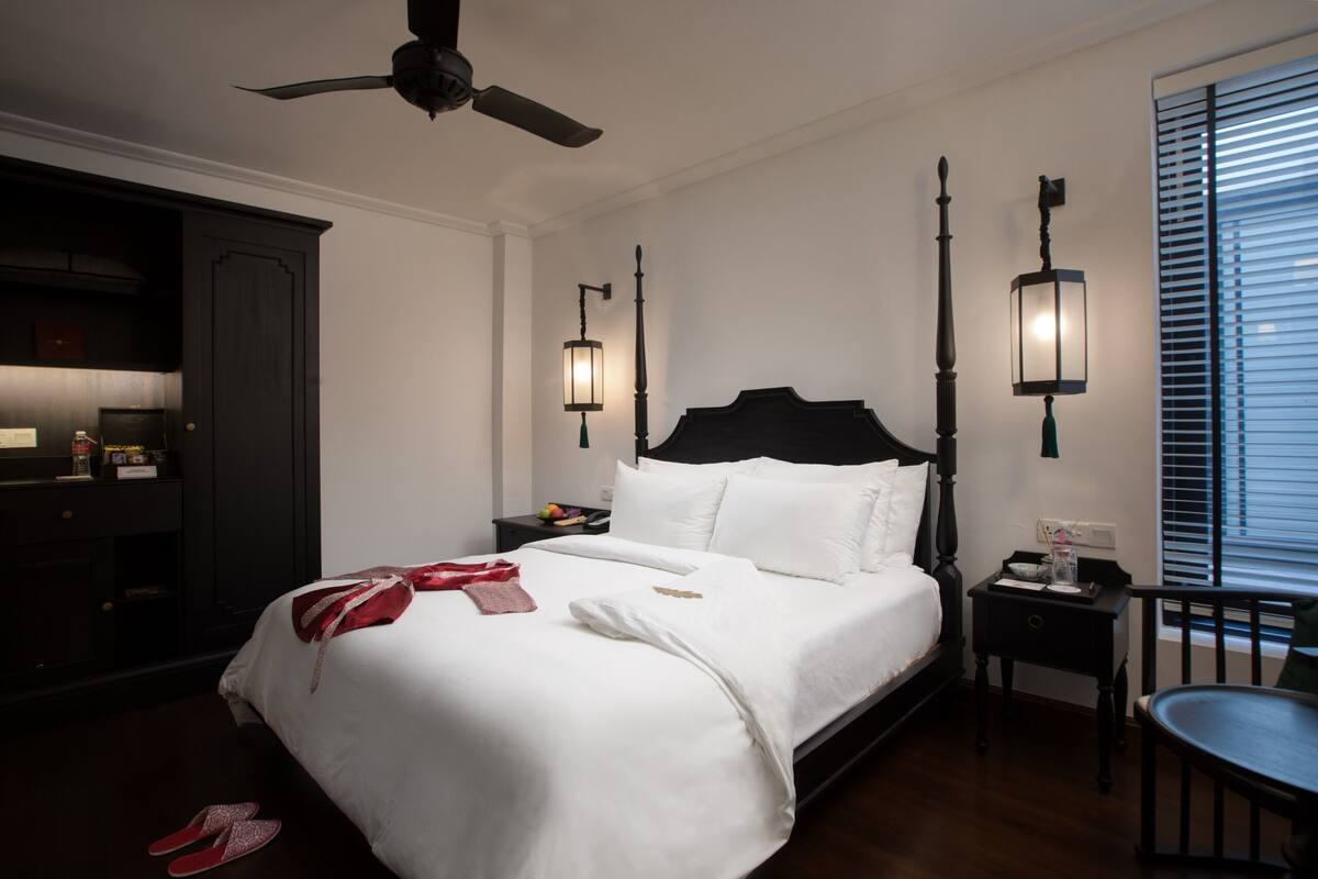 A neatly made bed with white linens, a dark wooden headboard, and two bedside tables with lamps.
