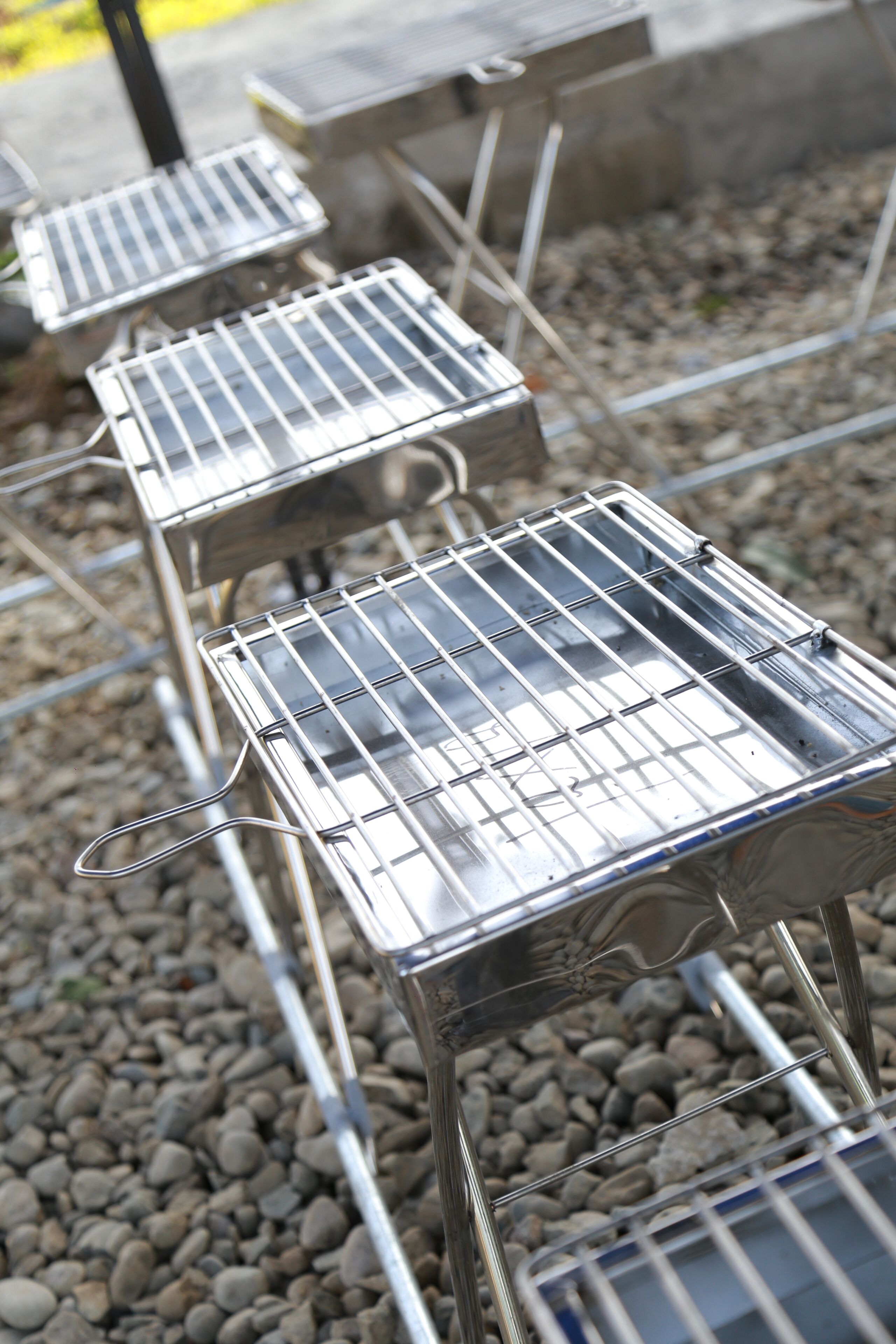 A row of metal barbecue grills on a gravel surface.