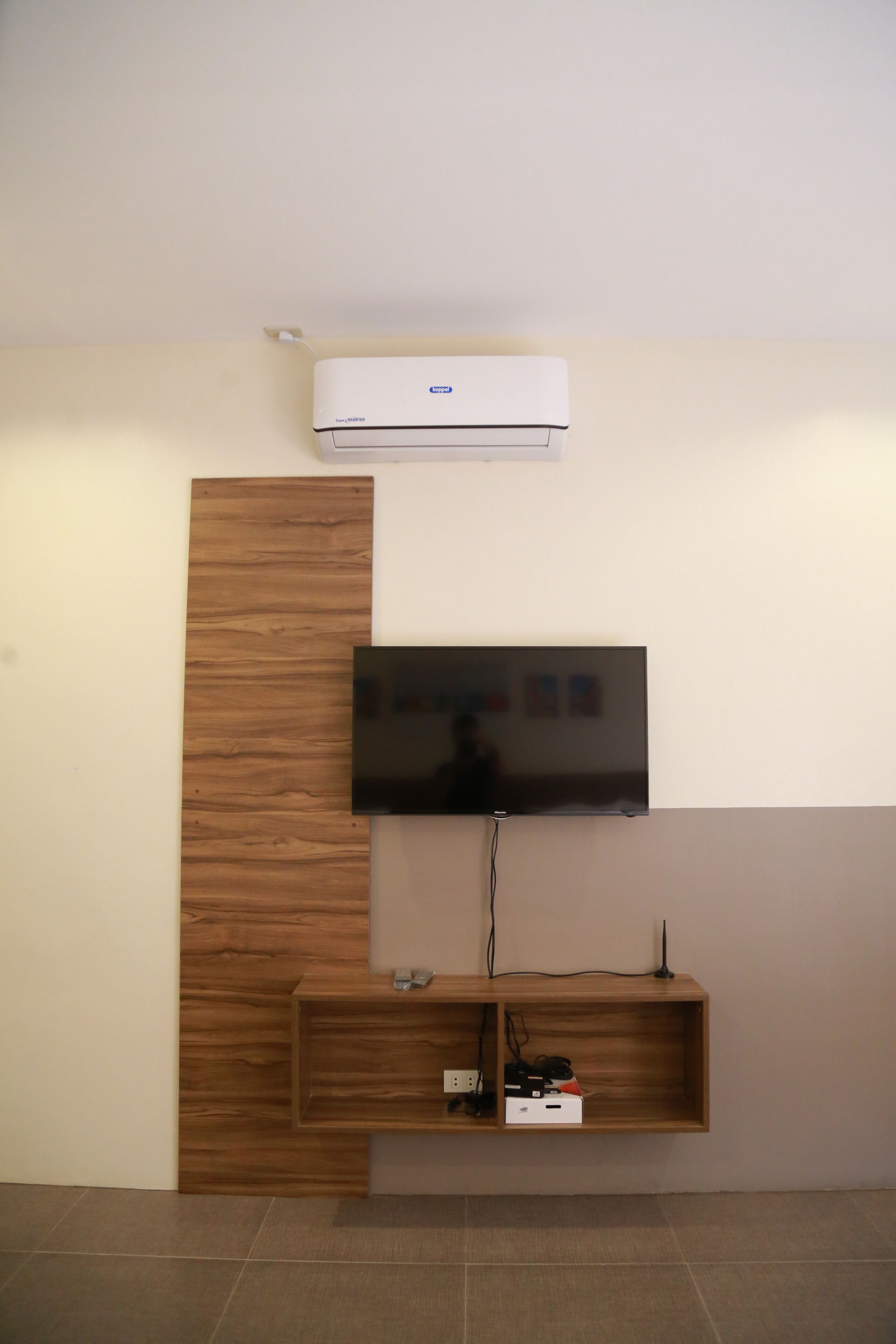 Un téléviseur à écran plat fixé au mur, avec un panneau en bois et une étagère intégrée en dessous.