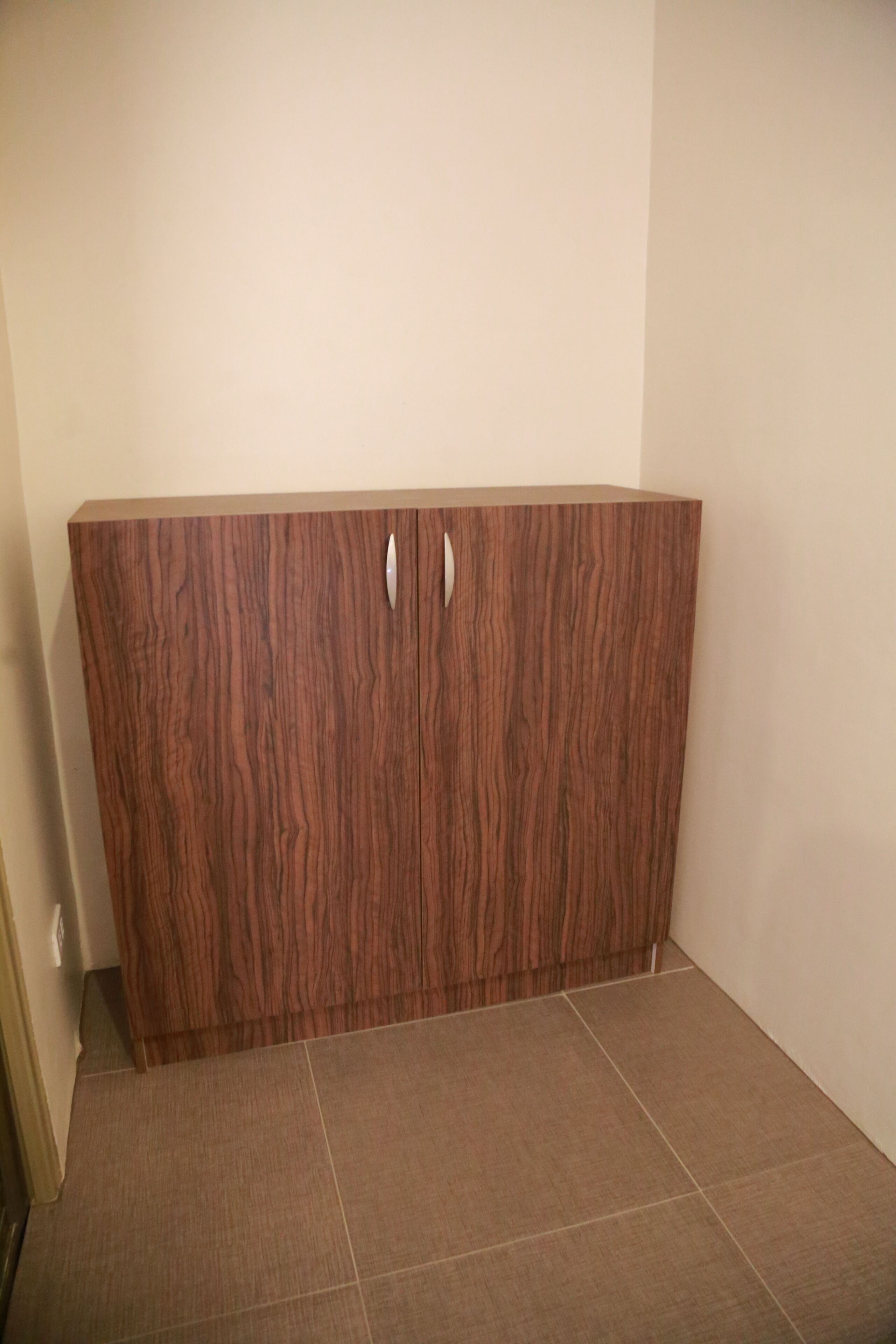 A corner room with a wooden wardrobe and tiled flooring.