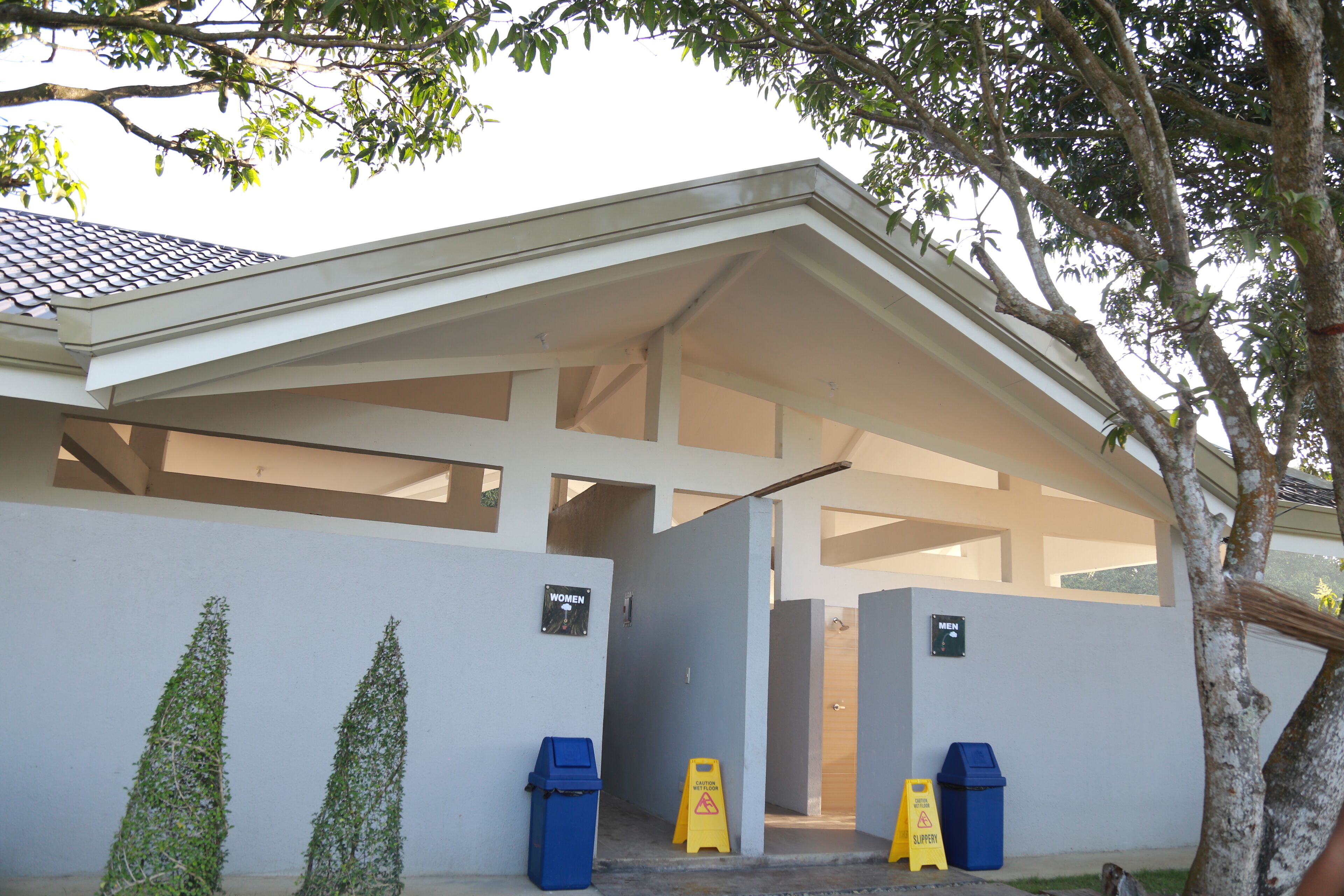 A building with a covered entrance, two trash bins, and signs indicating separate facilities for men and women.