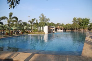 A large swimming pool with a modern structure in the center, surrounded by palm trees and greenery. - La Florentina Resort (Bustos)