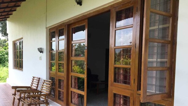 Eine überdachte Veranda mit Holzsesseln, Fliesenboden und einer Holztür mit Glasscheiben.
