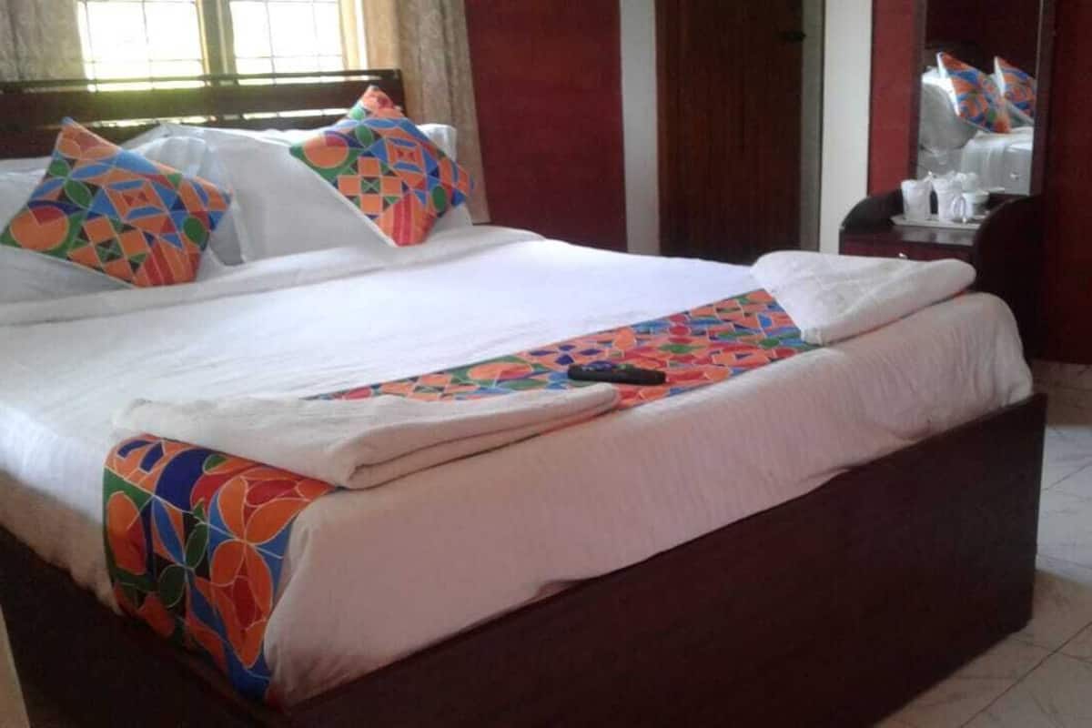 A neatly made bed with colorful pillows and a patterned blanket, a bedside table with a lamp, and a mirror on the wall.
