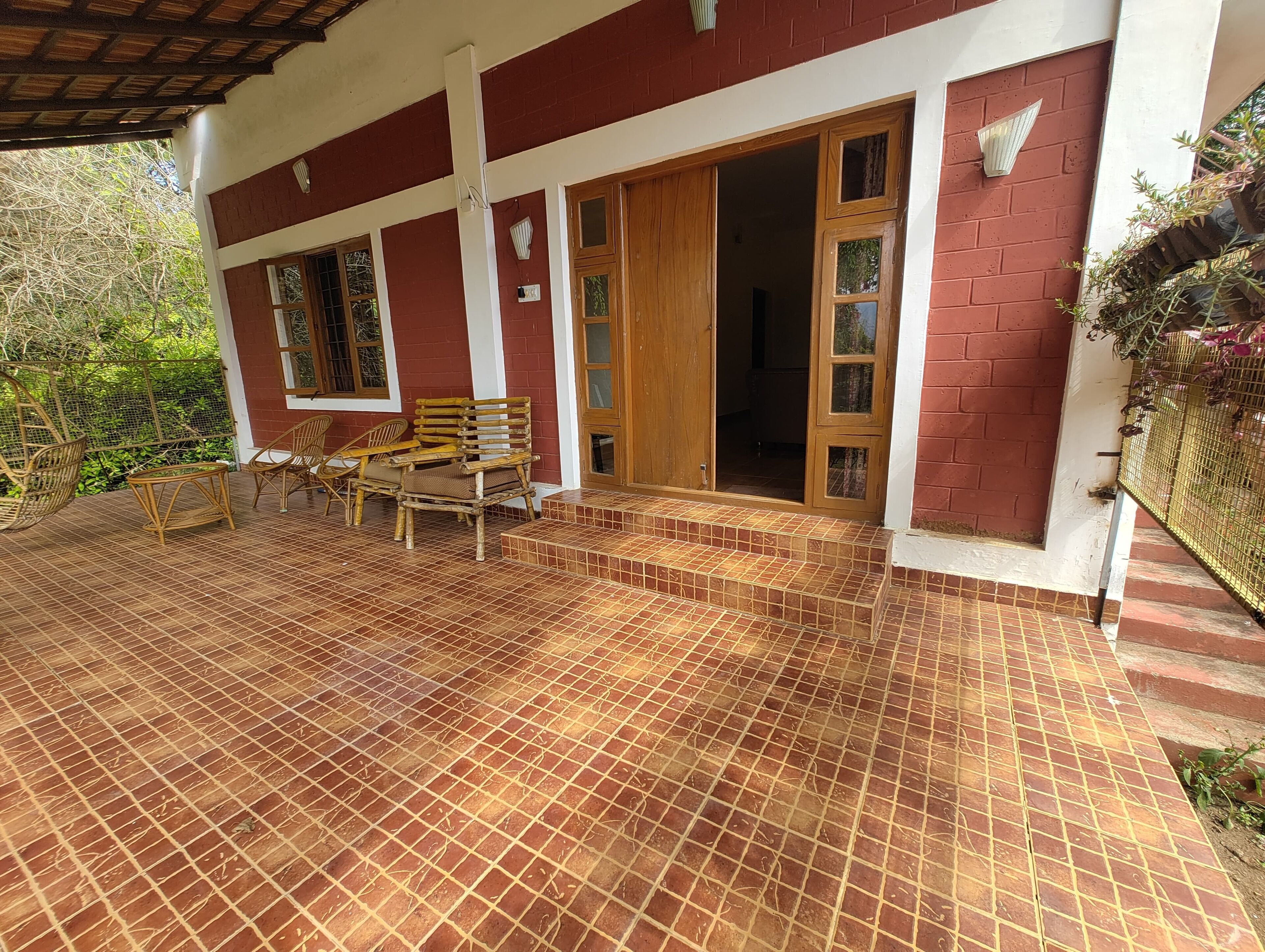 A covered patio with tiled flooring, wicker furniture, and a wooden door leading inside.