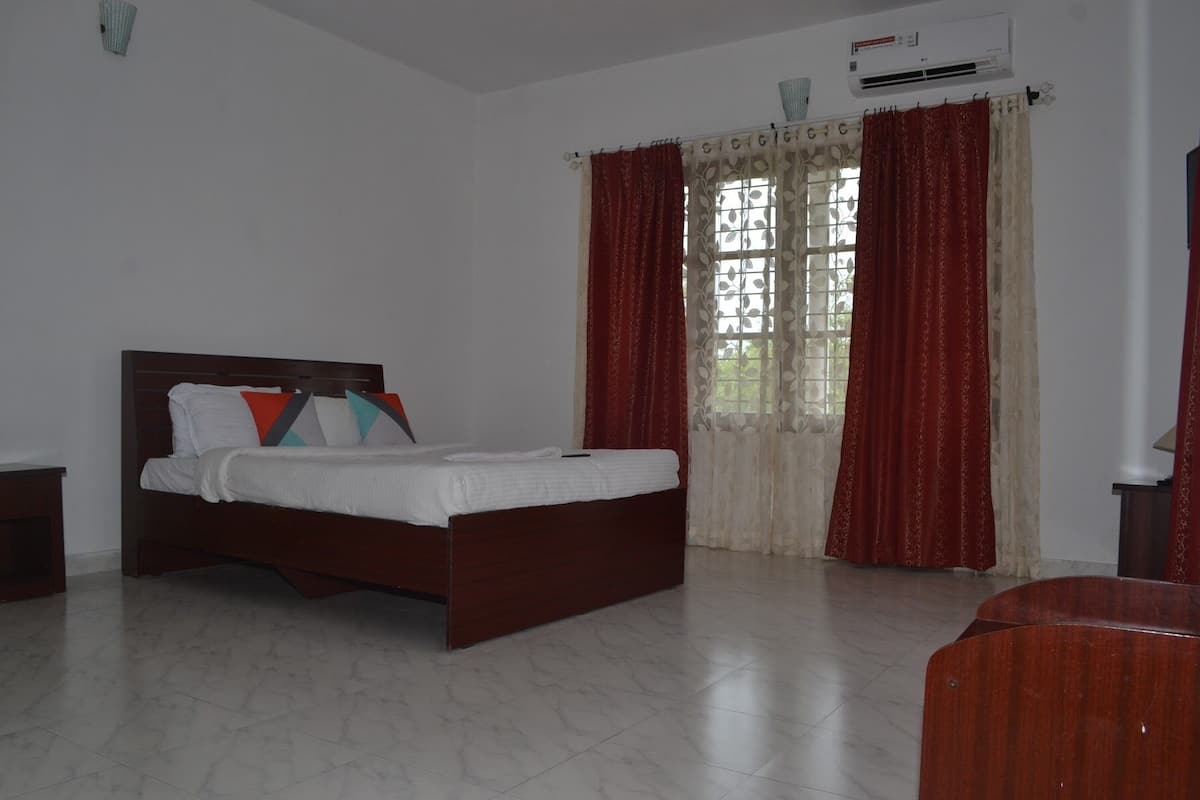 A bedroom with a bed, a nightstand, a window with curtains, and an air conditioning unit.