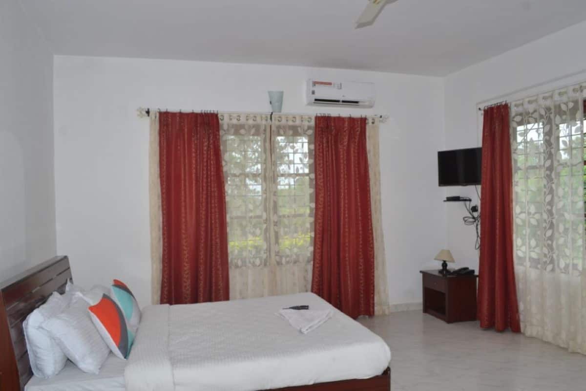 A hotel room with a bed, a TV on the wall, an air conditioner, and a window with curtains.