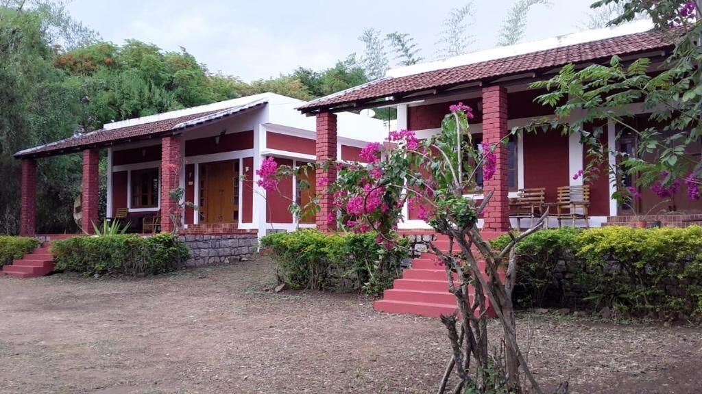 A two-story building with a red and white exterior, a covered porch with benches, and a small garden area with pink flowers.